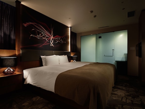 A hotel room with a large bed, a nightstand with a lamp, a wall art piece, and a sliding door closet.