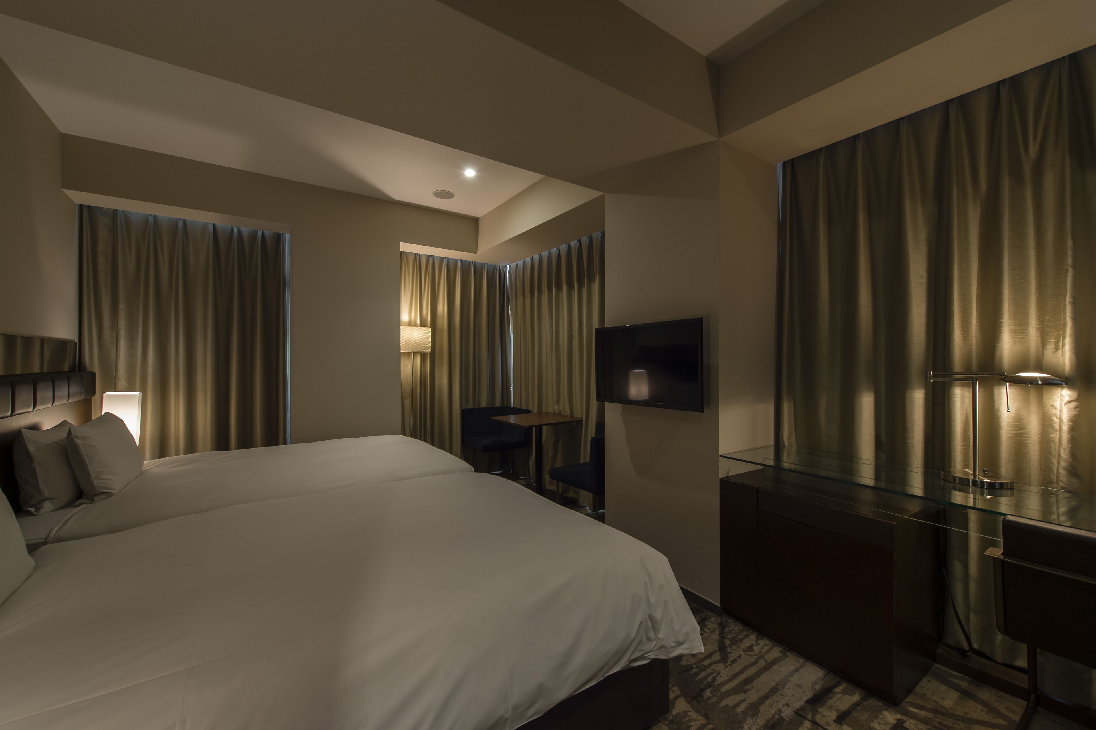 A modern hotel room with a large bed, a desk, a TV, and a glass partition.