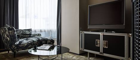 A modern hotel room with a large flat-screen TV, a patterned sofa, and a glass coffee table.