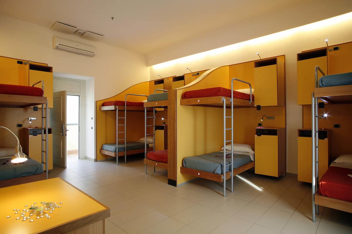 A dormitory room with bunk beds, a desk, and a chair.