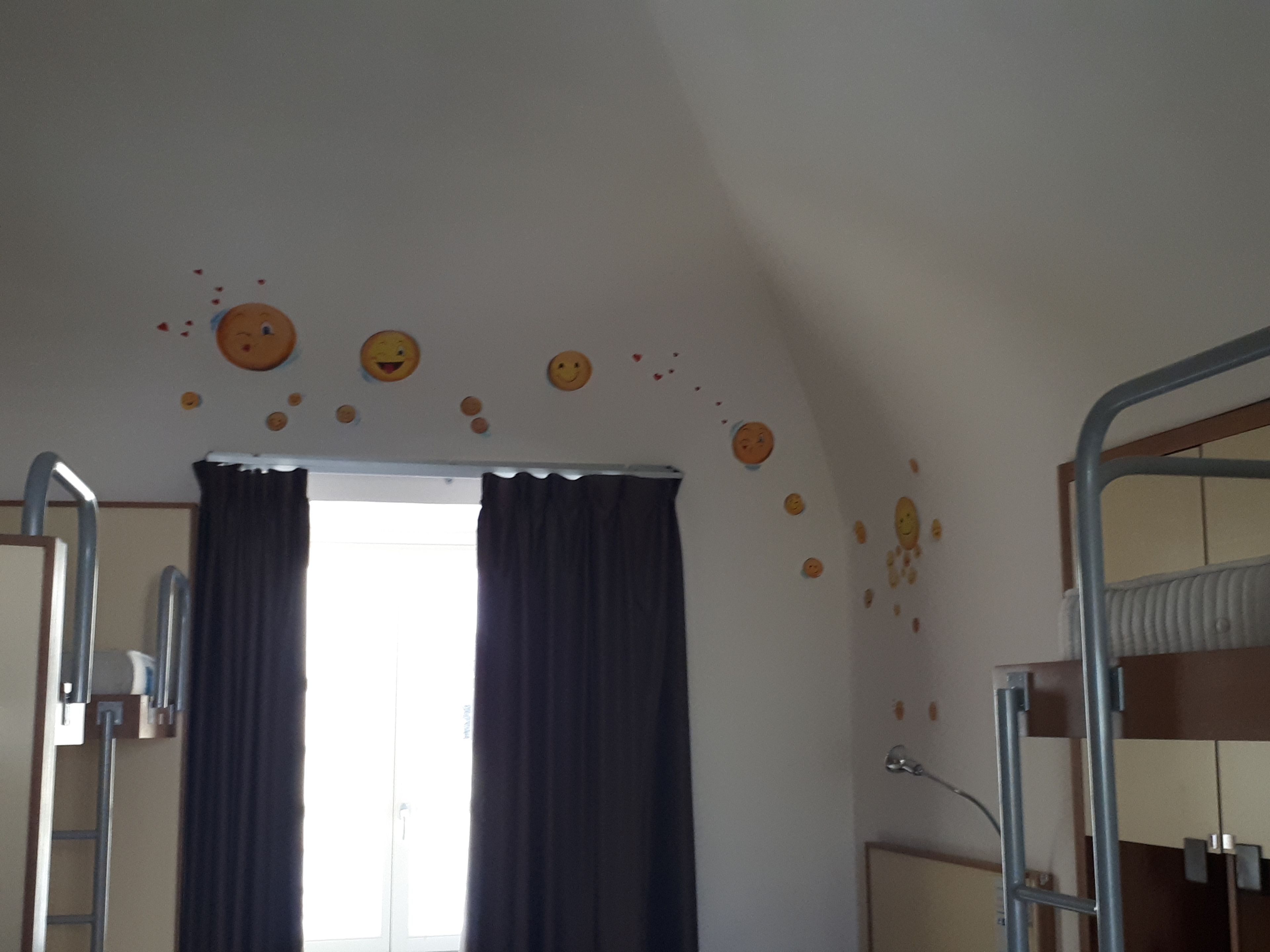 Una habitación con literas, una ventana con cortinas y decoraciones en la pared con caritas sonrientes.