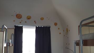 Una habitación con literas, una ventana con cortinas y decoraciones en la pared con caritas sonrientes.