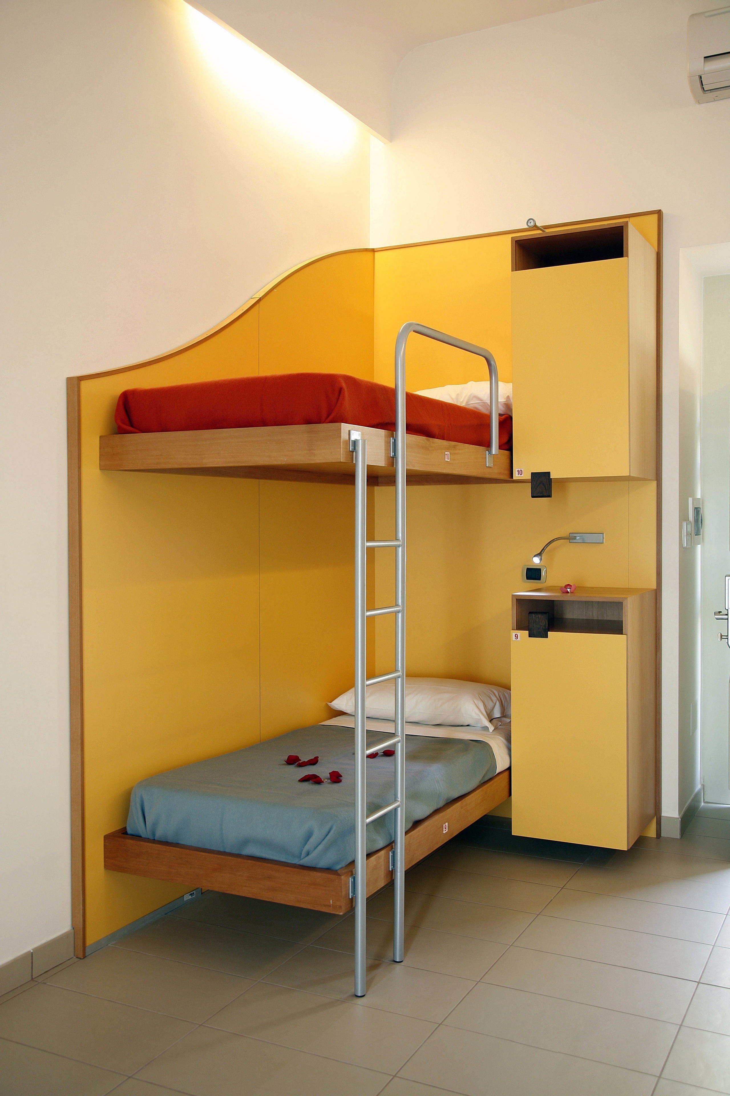 Una cama litera con escritorio y una escalera, un pequeño estante y una puerta.