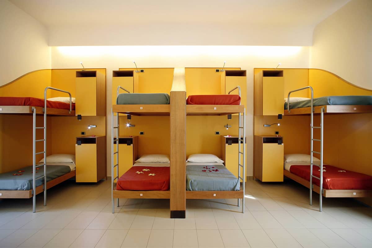 A dormitory room with bunk beds, each with a ladder, and a small desk with a chair.