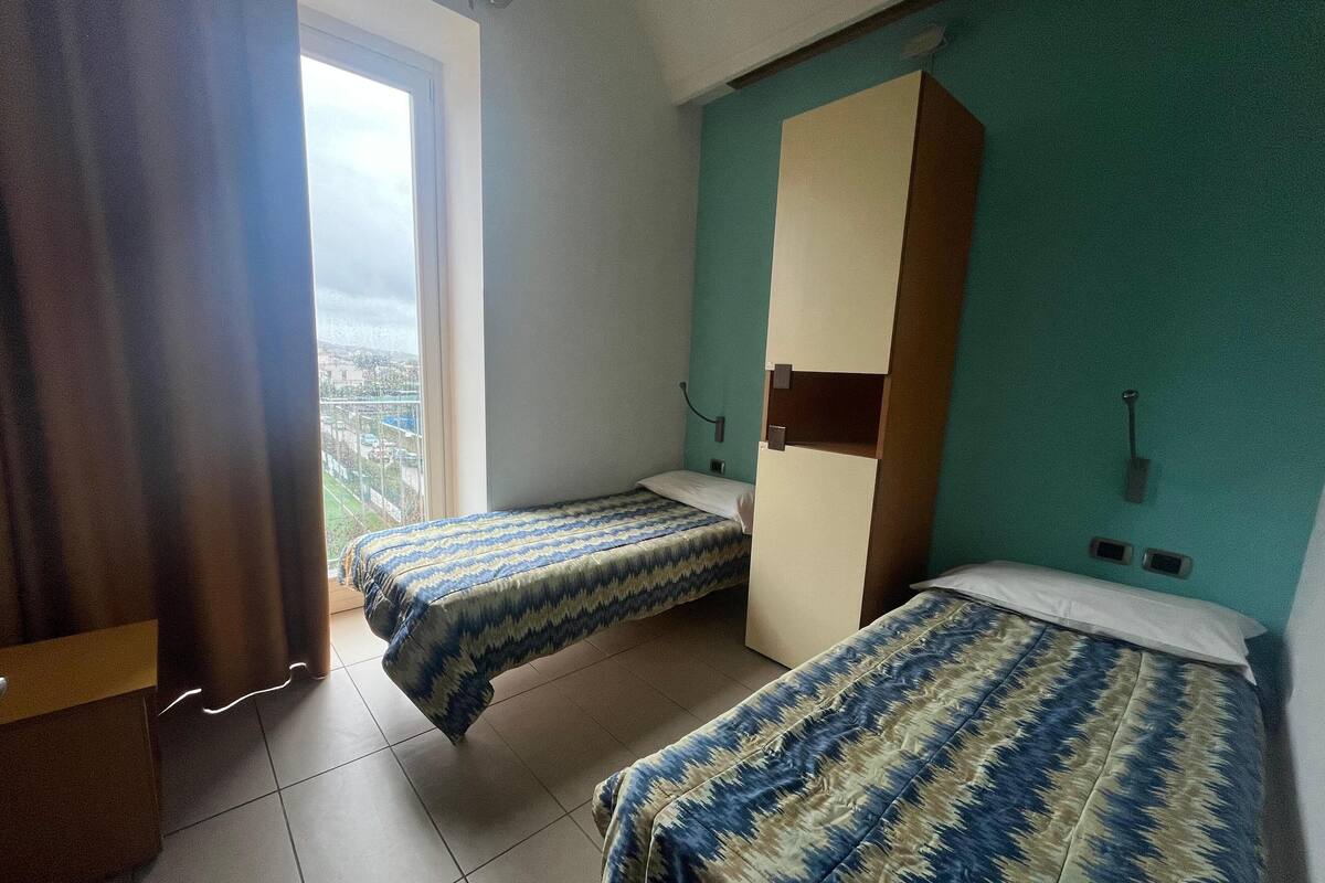A room with two beds, a window, and a view of the city.