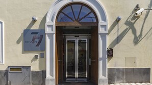Una entrada de edificio con puerta de cristal, un cartel encima y una cámara de seguridad en la pared.