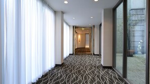 A hotel corridor with patterned carpet, large windows, and a view of an outdoor area. - Hotel Riverge Akebono (Fukui)