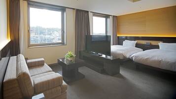 Una habitación de hotel con sofá, dos camas, televisión y ventana con cortinas.