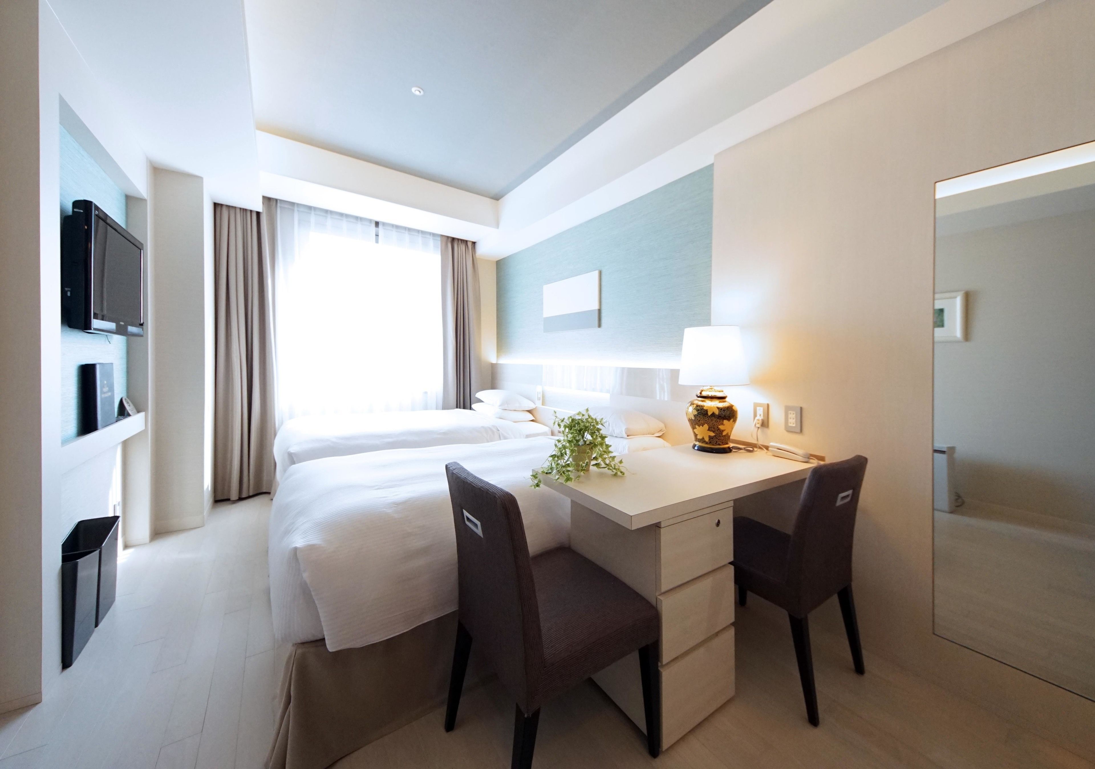 A hotel room with a bed, a desk with two chairs, a TV, and a lamp.