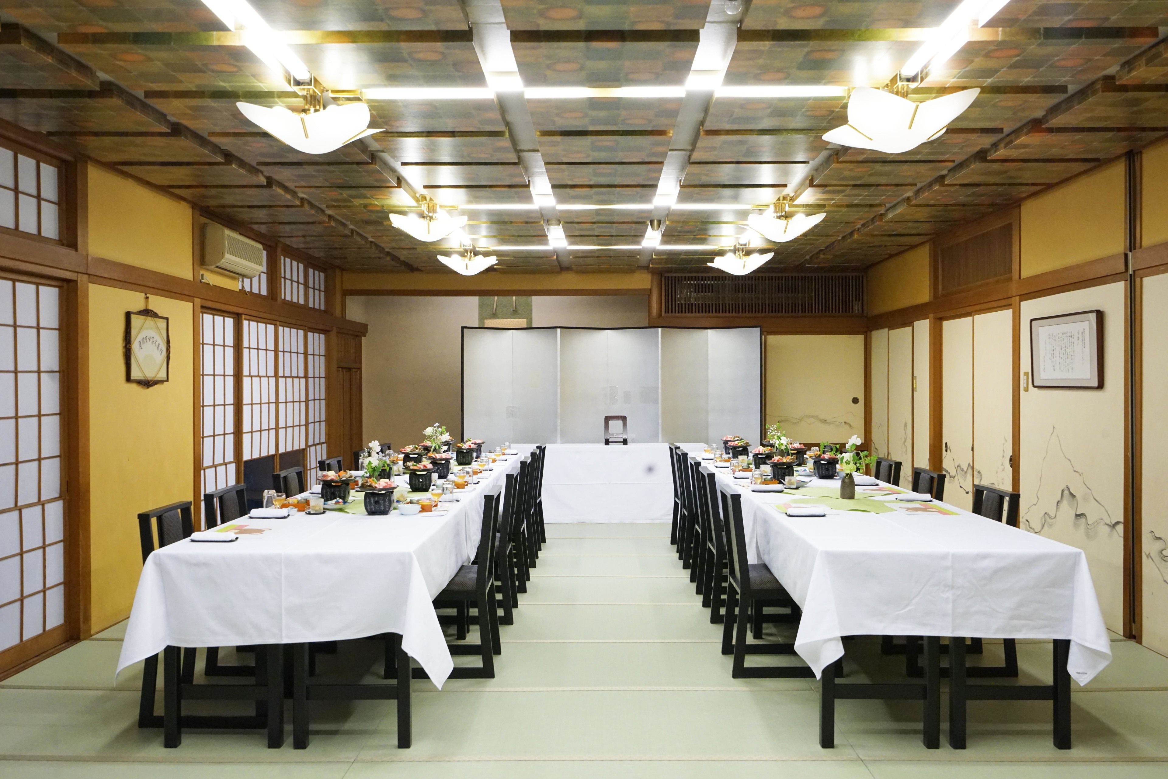 A conference room with long tables set for a meeting, equipped with chairs and tables, and a ceiling with light fixtures.