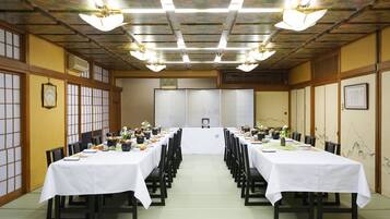 A conference room with long tables set for a meeting, equipped with chairs and tables, and a ceiling with light fixtures.