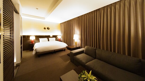A hotel room with a bed, a sofa, a nightstand, and a lamp. - Hotel Riverge Akebono (Fukui)