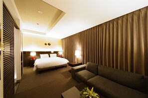 A hotel room with a bed, a sofa, a nightstand, and a lamp.