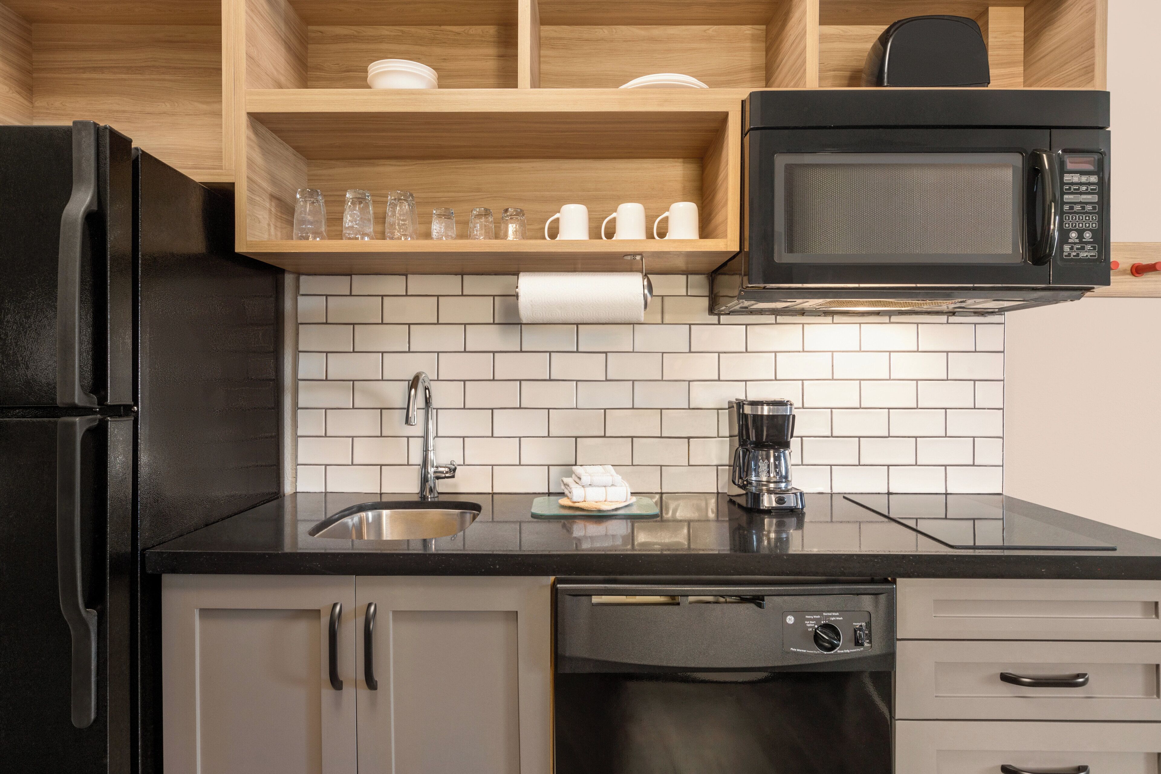 A modern kitchen with a black refrigerator, stainless steel sink, and a built-in microwave.