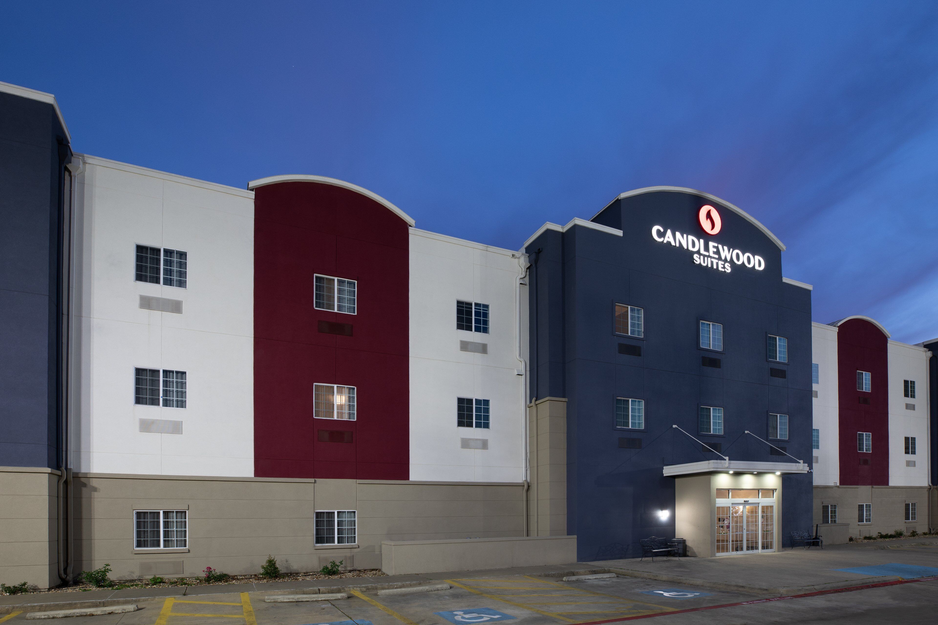 A multi-story hotel with a prominent "Candlewood Suites" sign, a parking lot with handicapped parking, and a flat roof design.