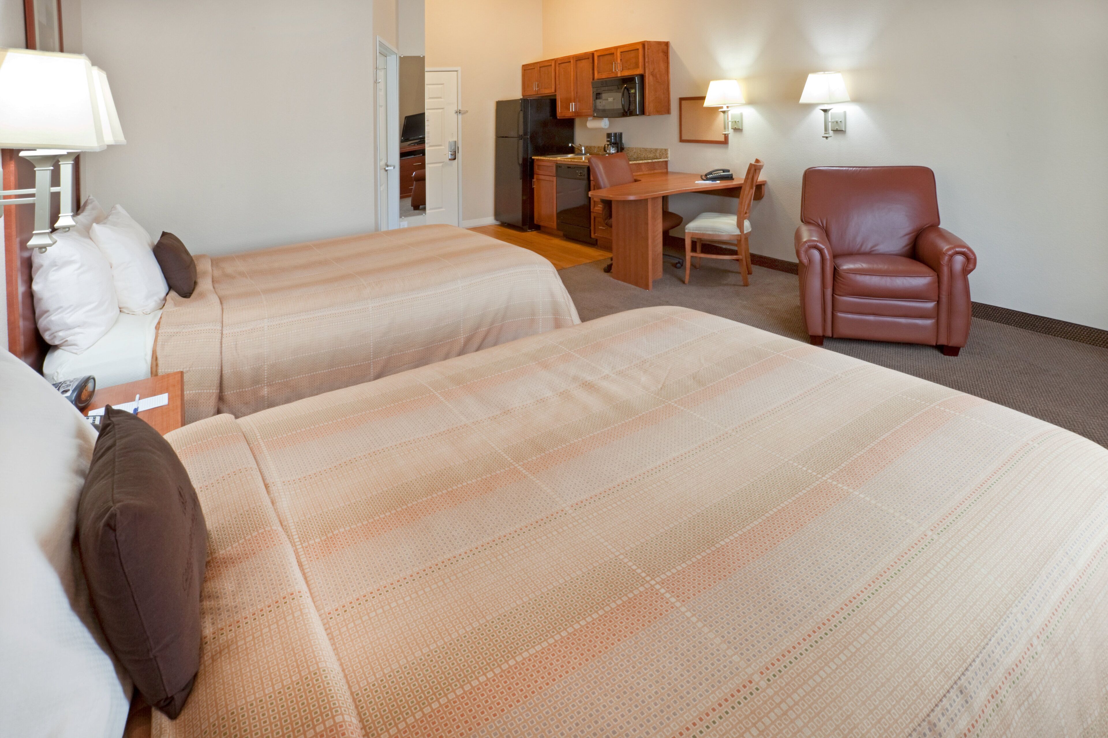 Ein Hotelzimmer mit zwei Betten, einem Schreibtisch, einem Stuhl und einer Küchenzeile.
