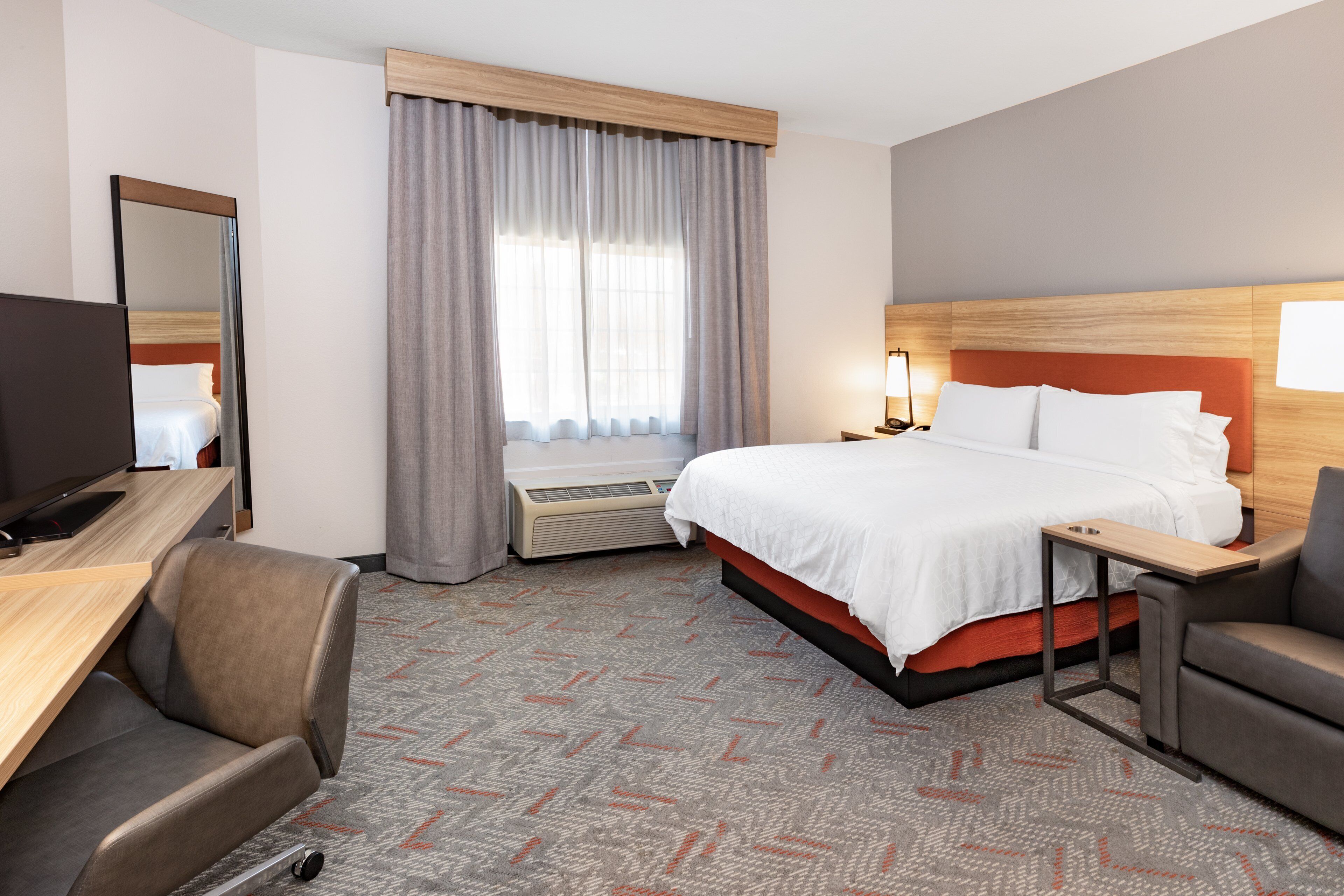 A hotel room with a bed, a desk, a chair, a TV, and a window with curtains.