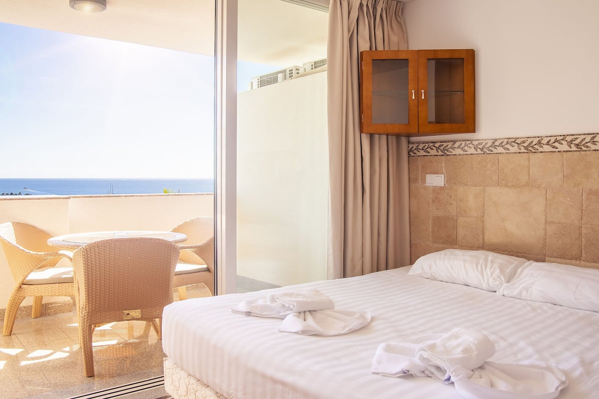 A hotel room with a bed, a small table, and chairs, a sliding glass door to the outside, and a wooden cabinet.