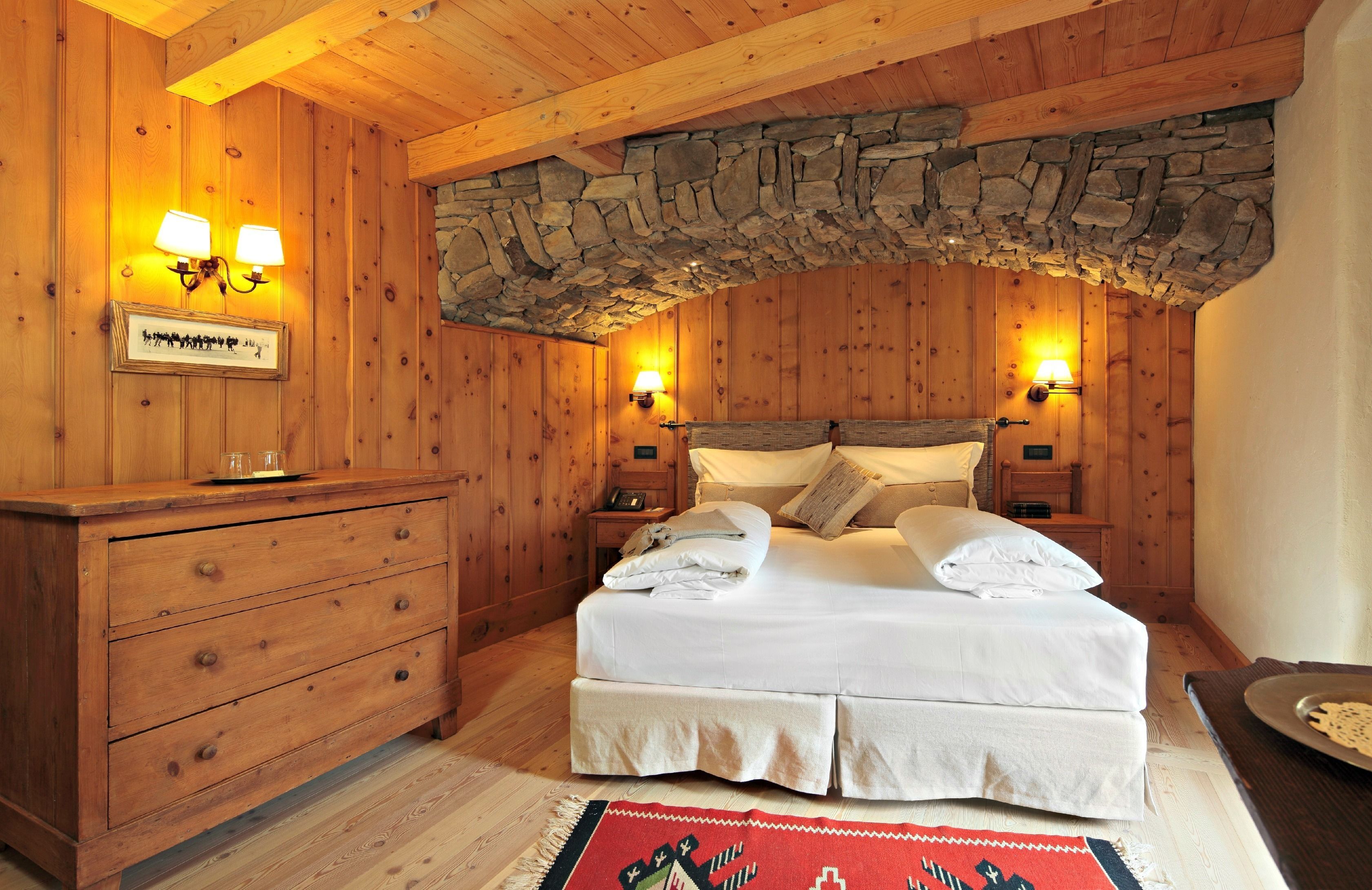 Camera da letto con pannelli in legno, soffitto a volta in pietra, un letto con lenzuola bianche, due lampade da comodino e un comò in legno.