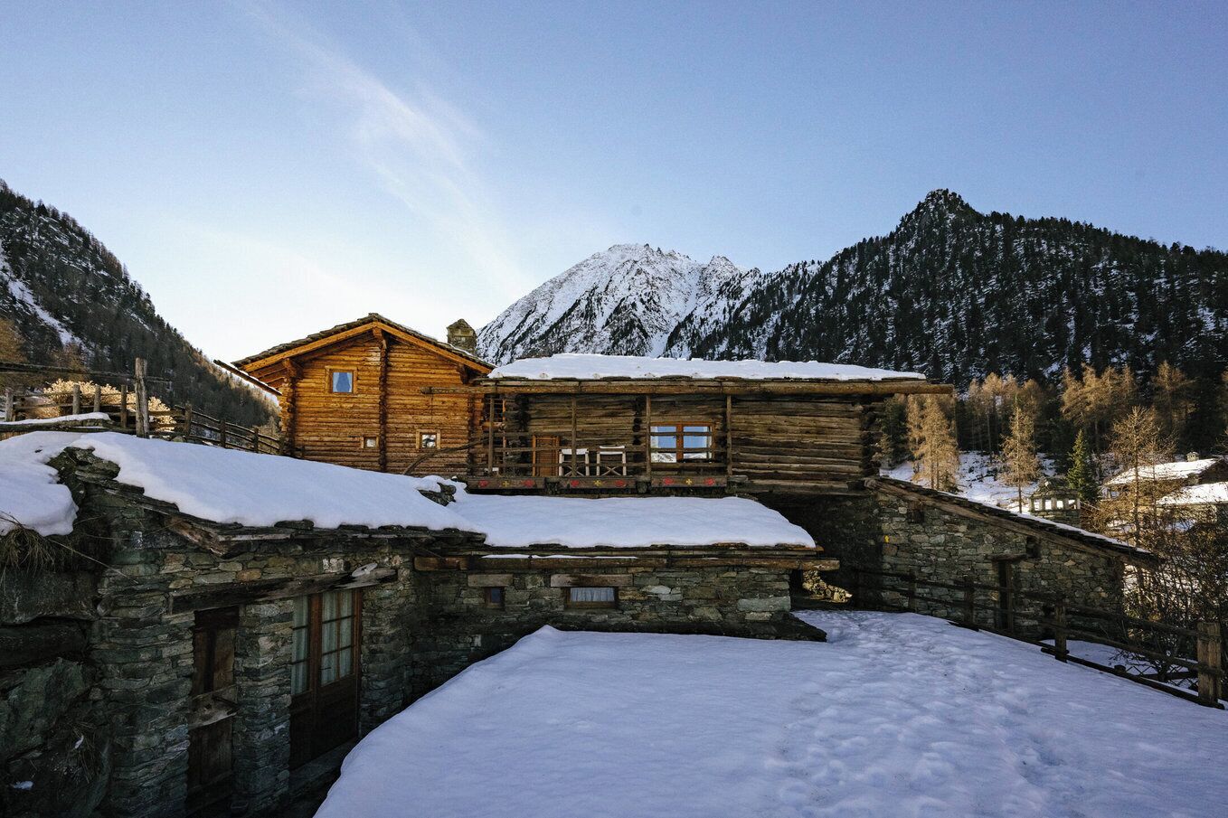 Une cabane en rondins avec un pont de pierre, située dans une région montagneuse enneigée.