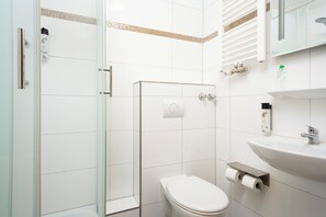 Een moderne badkamer met een douchecabine van glas, een toilet, een wastafel en een spiegel.