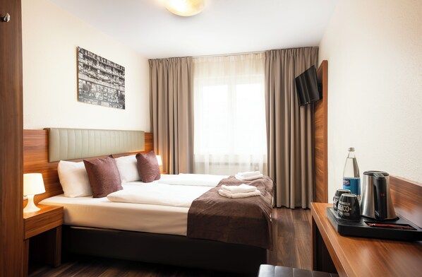 Een hotelkamer met een bed, een nachtkastje met een lamp, een flatscreen televisie aan de wand en een raam met gordijnen.