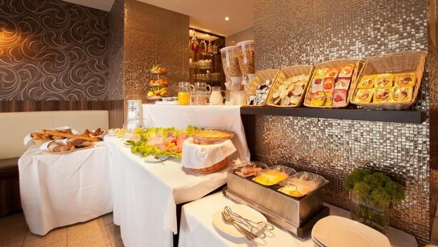 Ein reichhaltiges Buffet mit verschiedenen Speisen, darunter Obst, Gebäck und Getränke, präsentiert auf Tischen und Regalen.