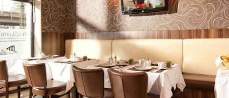 Un restaurant avec des banquettes et des tables, un téléviseur fixé au mur et un papier peint à motifs.