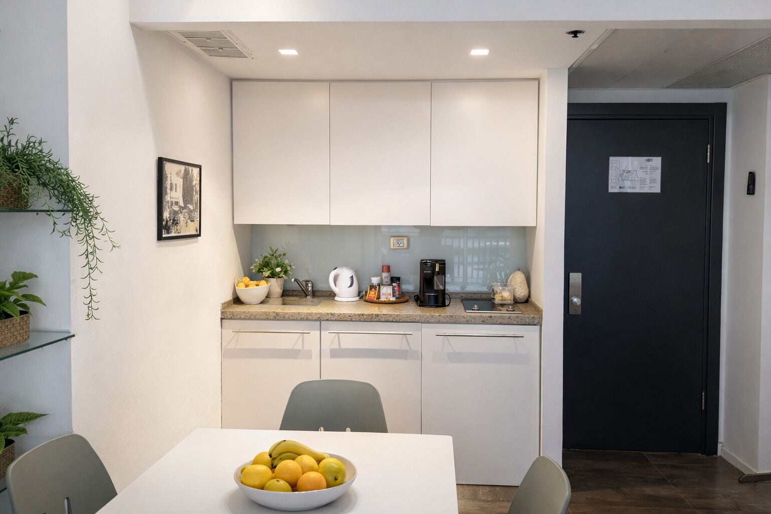 A modern kitchen with white cabinets, a coffee maker, and a bowl of fruit on the counter.