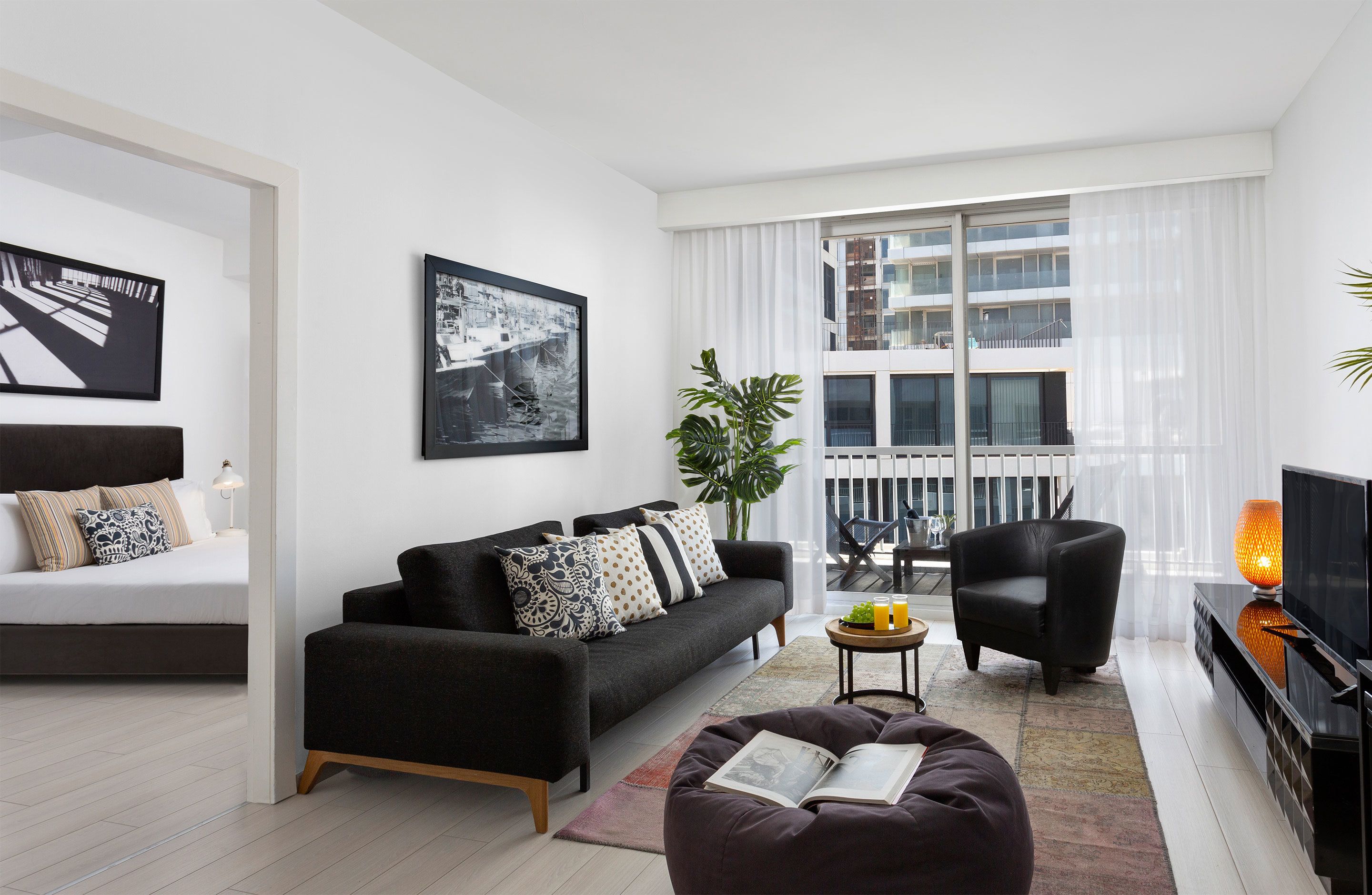 Ein modernes Wohnzimmer mit einer Couch, einem Sessel, einem Fernseher und einem Balkon mit großen Fenstern.