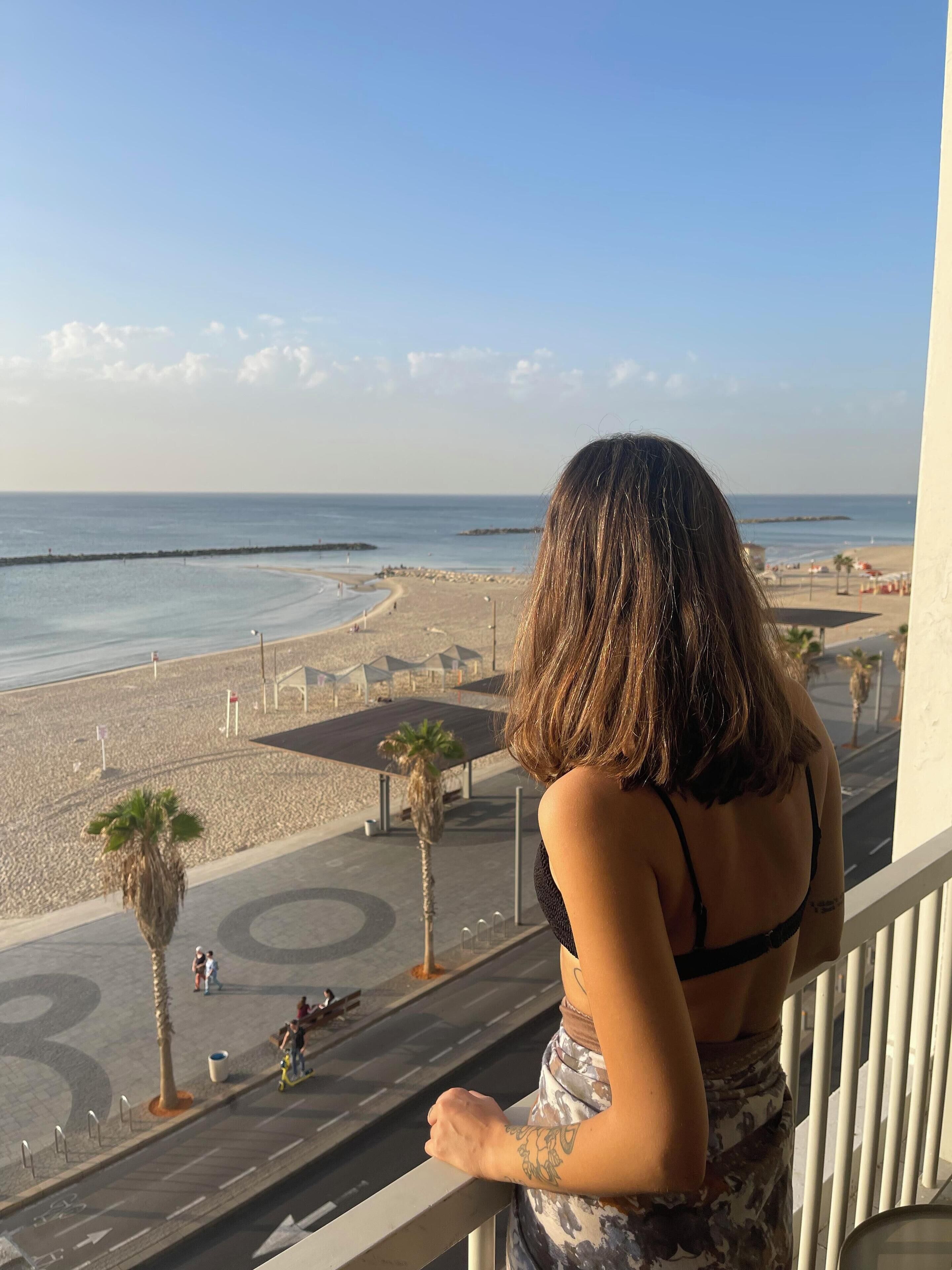 A balcony with a view of a beach and a road with palm trees and people.