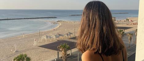 A balcony with a view of a beach and a road with palm trees and people.