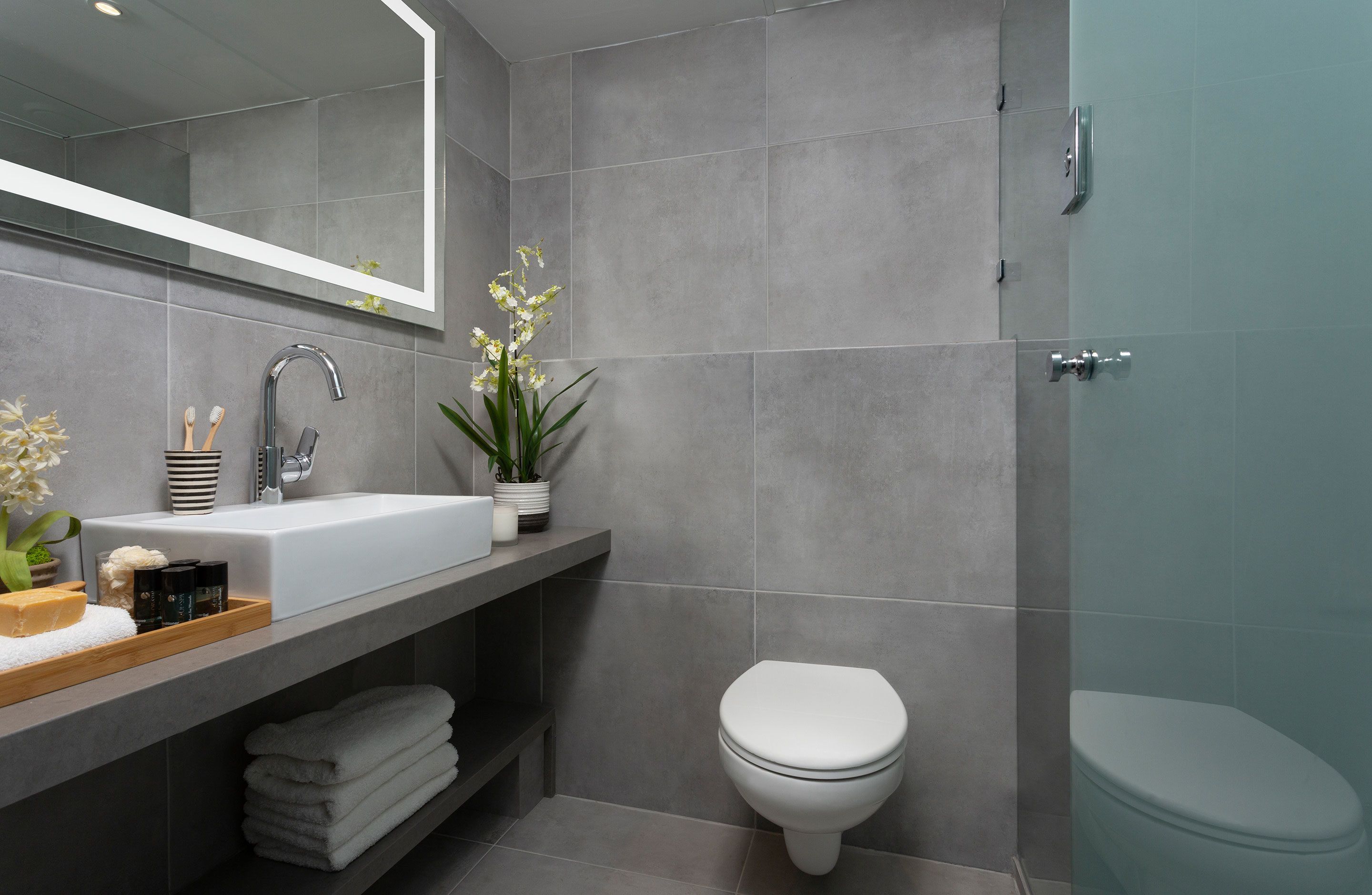 A modern bathroom with a large mirror, a white sink, a toilet, and a shower area.