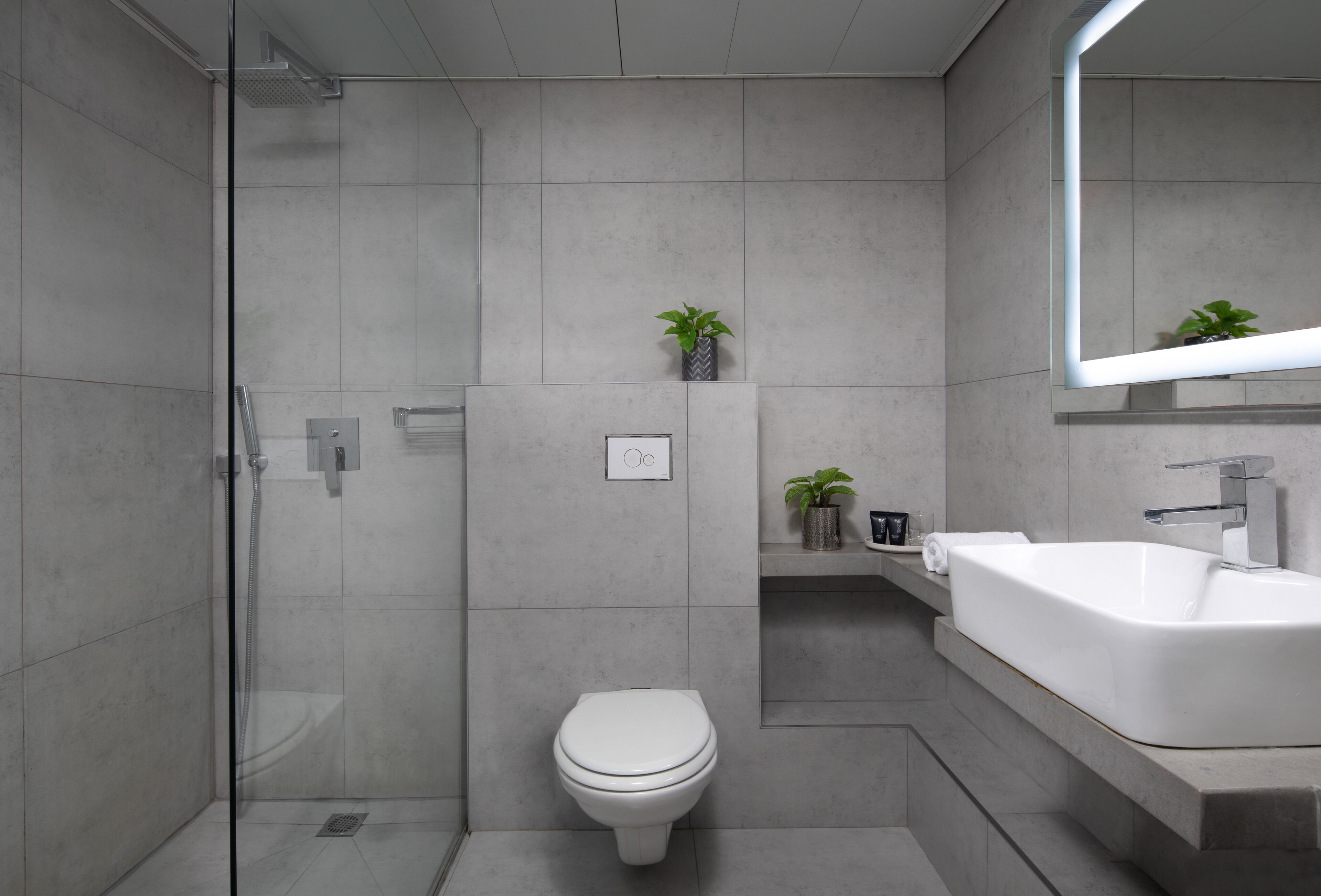 A modern bathroom with a glass shower enclosure, a white toilet, and a large sink with a mirror above it.
