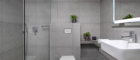 A modern bathroom with a glass shower enclosure, a white toilet, and a large sink with a mirror above it.