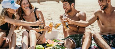 A group of people sitting on a beach with drinks and snacks.