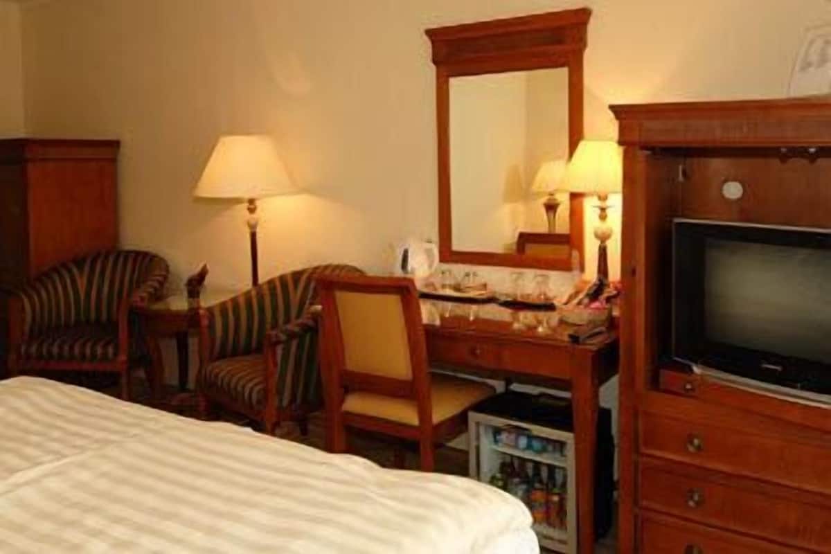 Habitació d'hotel amb un llit, una taula de nit de fusta amb mirall, dues làmpades, una televisió i una cadira.