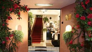 L’entrée d’un hôtel, avec un tapis rouge menant à un escalier, le tout agrémenté de fleurs rouges et de verdure.