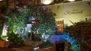 La façade d’un hôtel, ornée d’une enseigne indiquant « Hôtel Romantik », est entourée d’une végétation luxuriante et de plantes en fleurs.