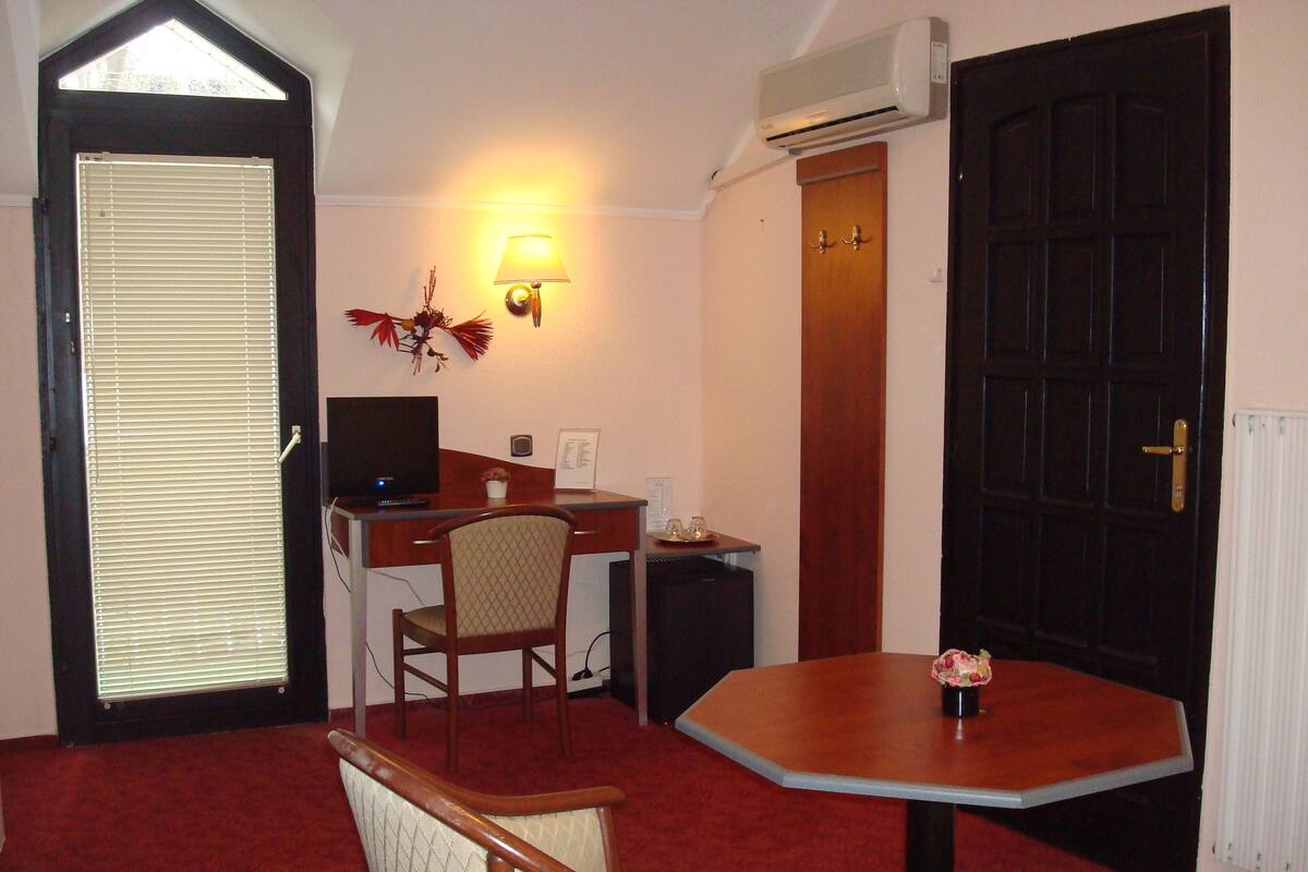 Habitació d'hotel amb escriptori, cadira, taula petita, làmpada penjada a la paret, porta i aparell d'aire condicionat.