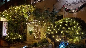 La façade d’un hôtel, avec une enseigne indiquant « HÔTEL » et un arbre décoratif illuminé de guirlandes lumineuses.