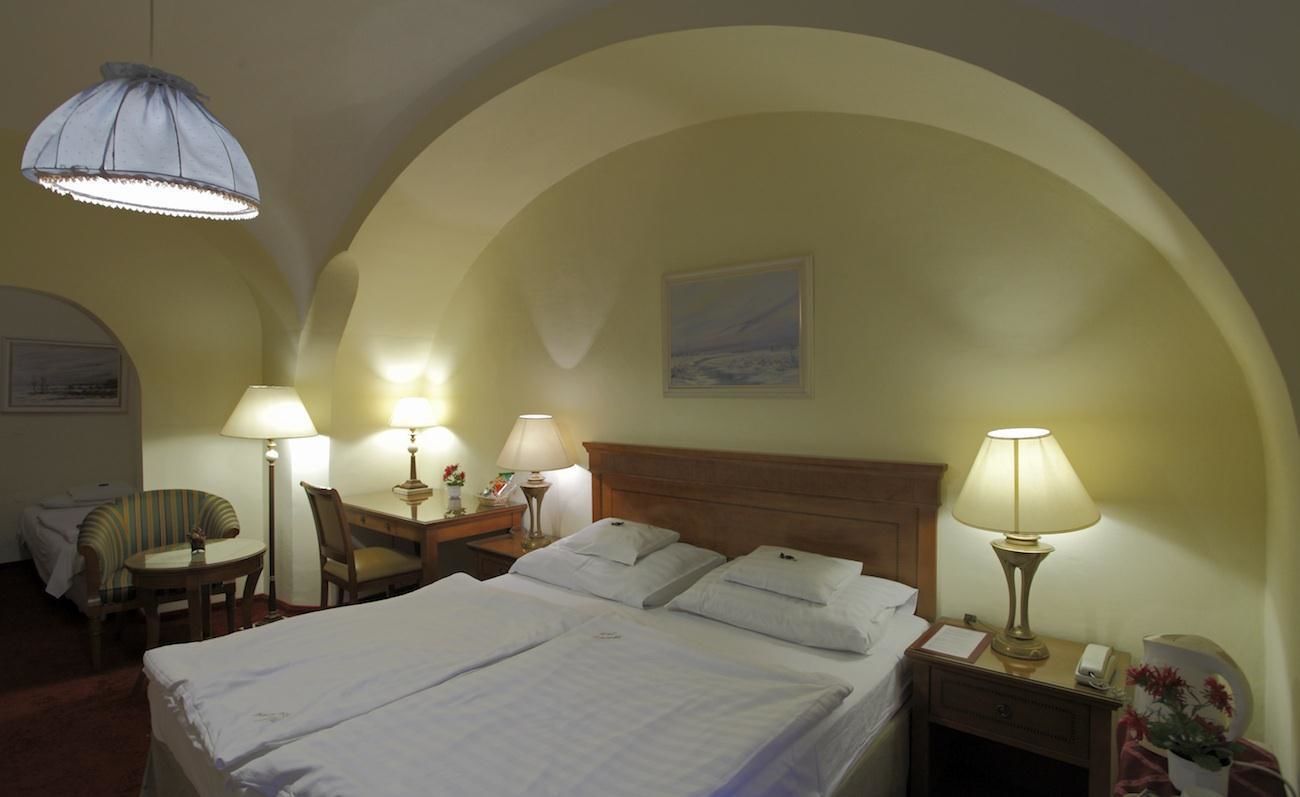 Una habitación de hotel con una cama grande, dos lámparas de noche, un escritorio con una silla y una mesita con lámpara.