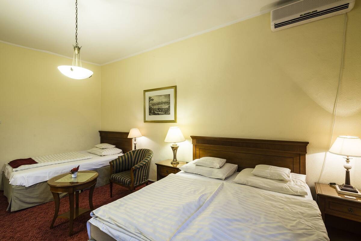 Habitació d'hotel amb dos llits individuals, una cadira, una taula petita i dues làmpades de nit.