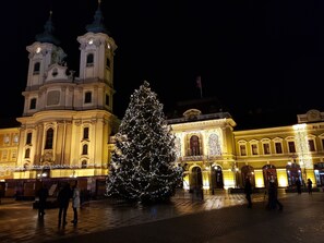 Un edificio storico con due torri di orologi, un grande albero di Natale e persone che passeggiano.