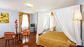 A hotel room with a bed, two chairs, a small table, a TV, and a painting on the wall.