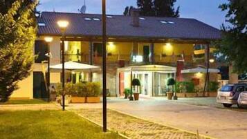 A hotel with a central entrance, a covered outdoor seating area, and a parking lot.