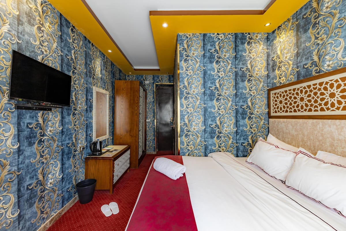 A hotel room with a large bed, a flat-screen TV, a wooden desk, and a red carpet.