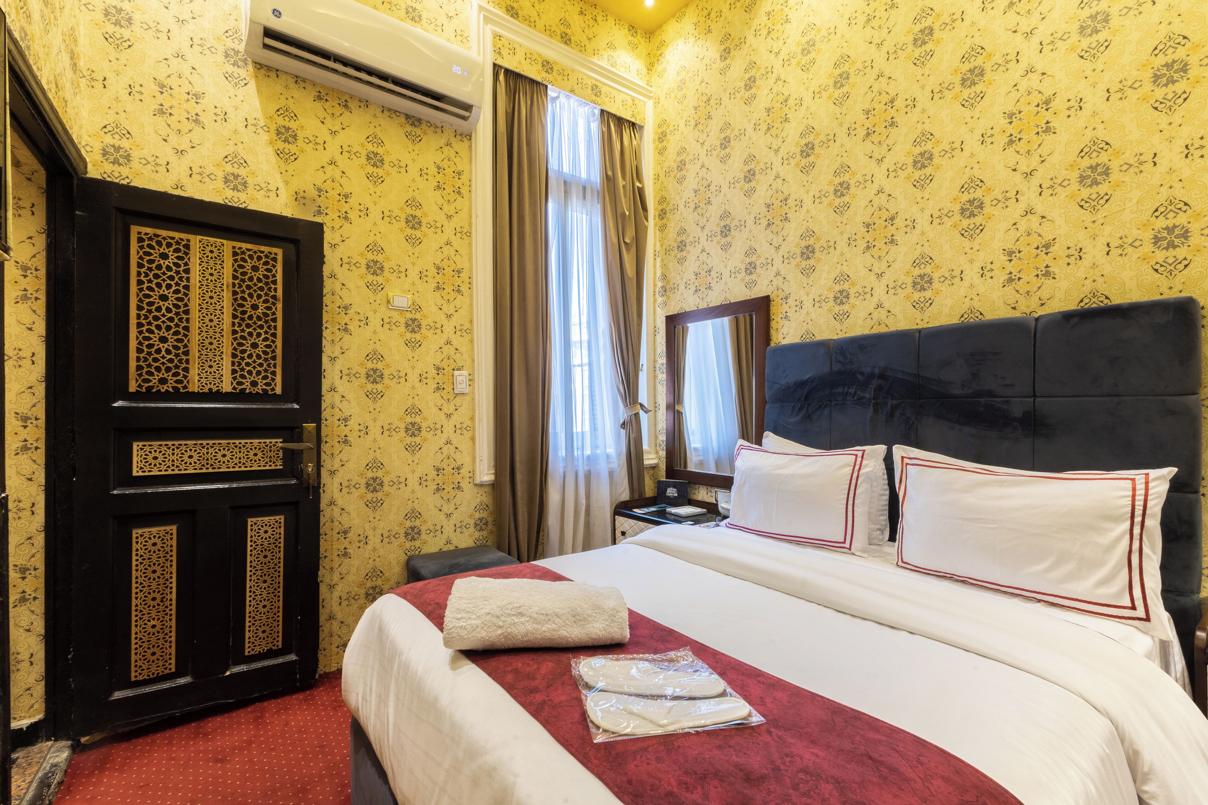 A hotel room with a bed, a nightstand, a mirror, and a door with intricate designs.