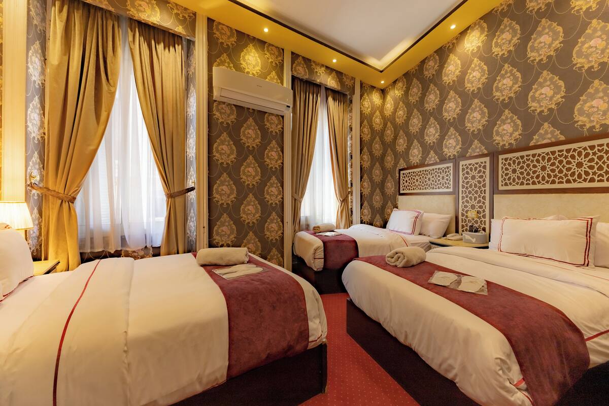 A hotel room with three beds, a large window with curtains, an air conditioning unit, and a decorative headboard.