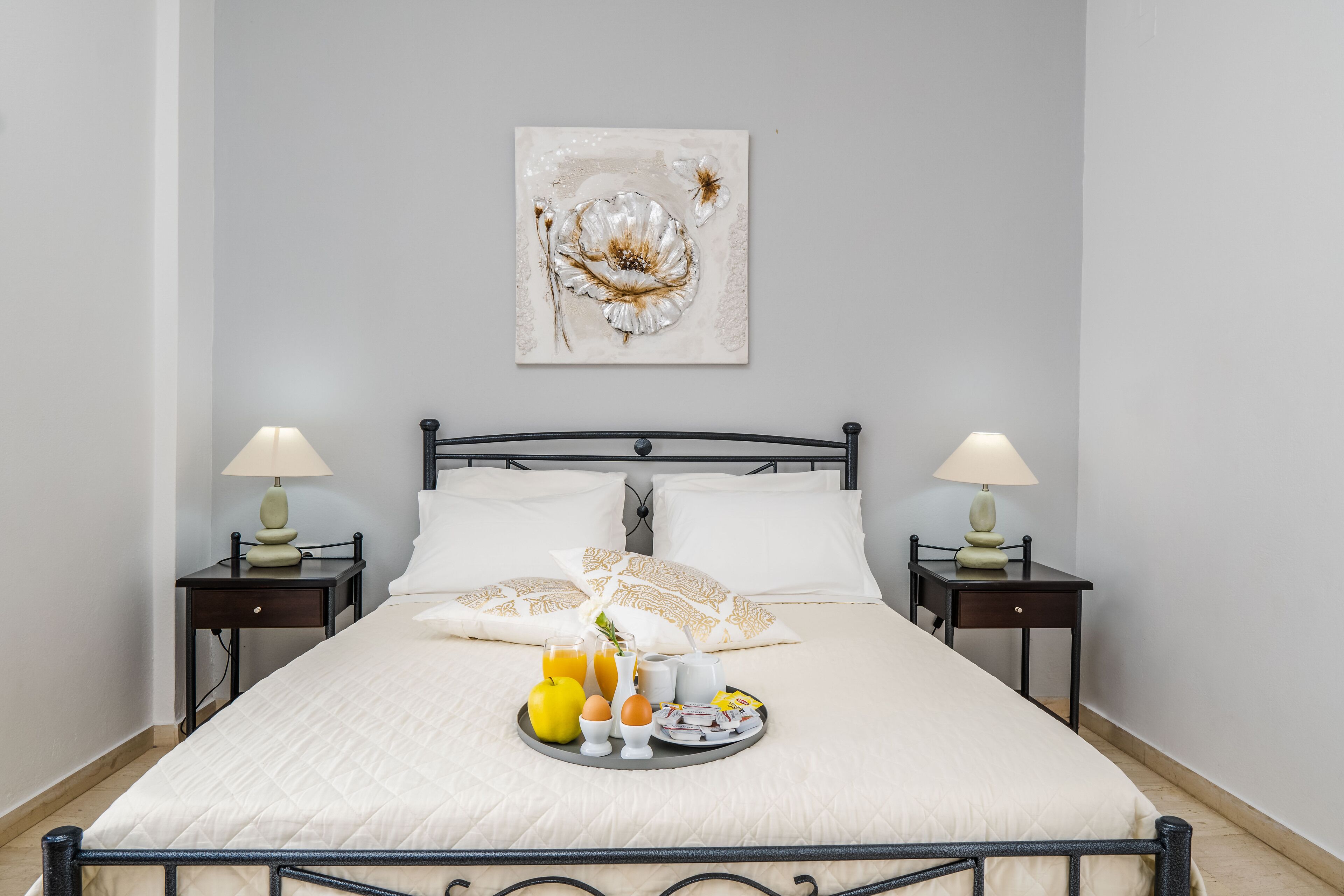A neatly made bed with a tray of breakfast items, two bedside lamps, and a decorative wall piece.